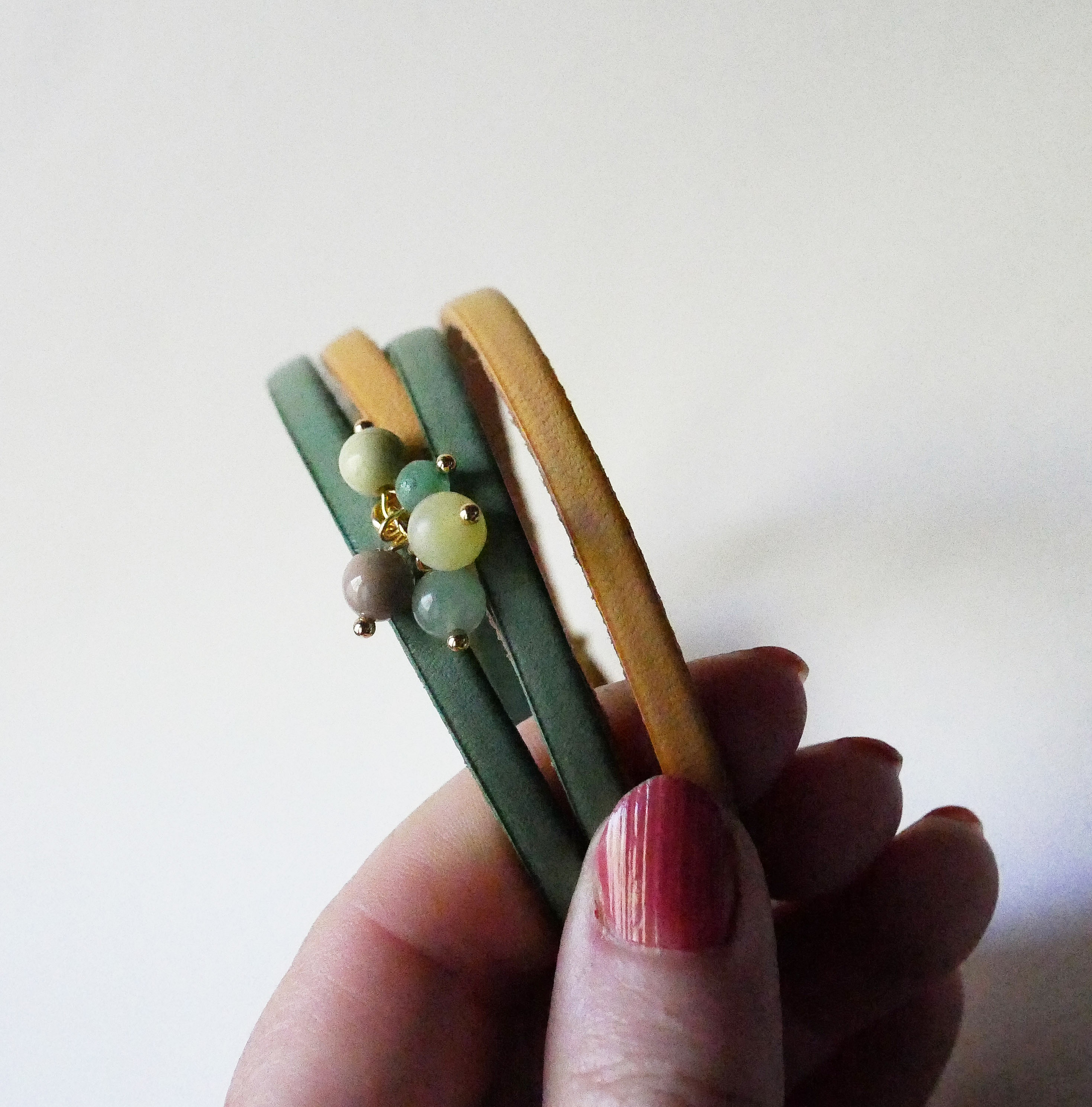 Dobbelt skinnarmb&aring;nd dekorert med myke, gr&oslash;nne perler og gullspenne