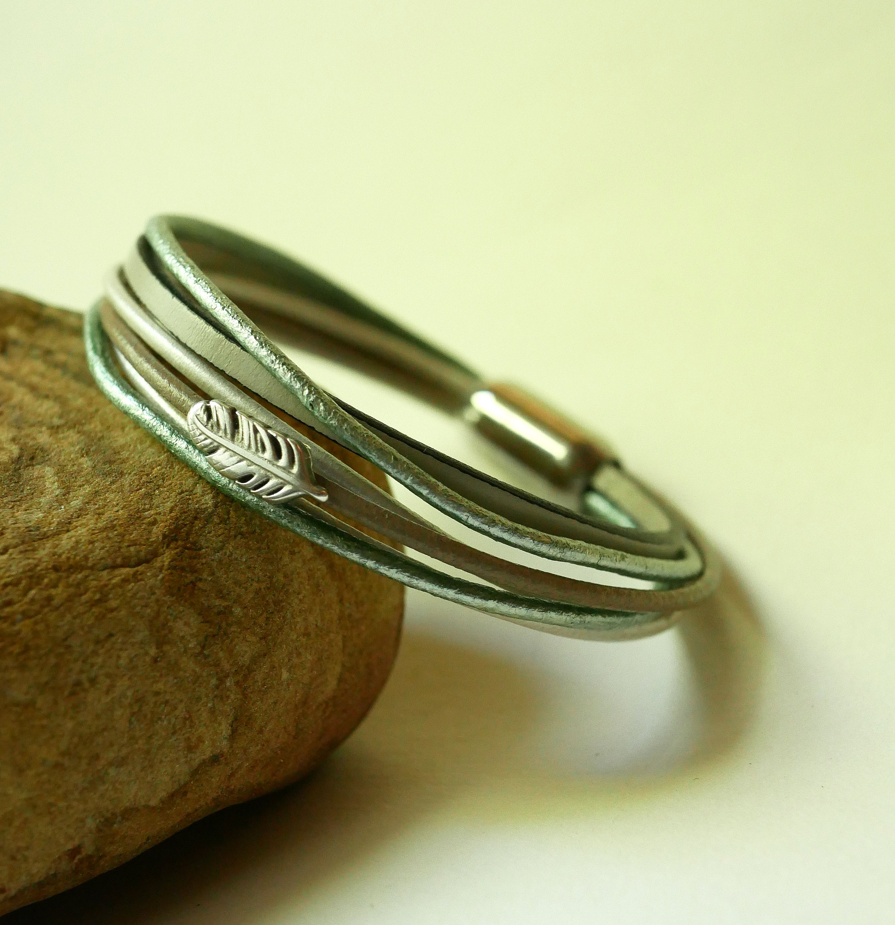 Armb&aring;nd i flere skinnfarger i beige, lysegr&oslash;nne og perlemorfargede nyanser, dekorert med en liten fj&aelig;r