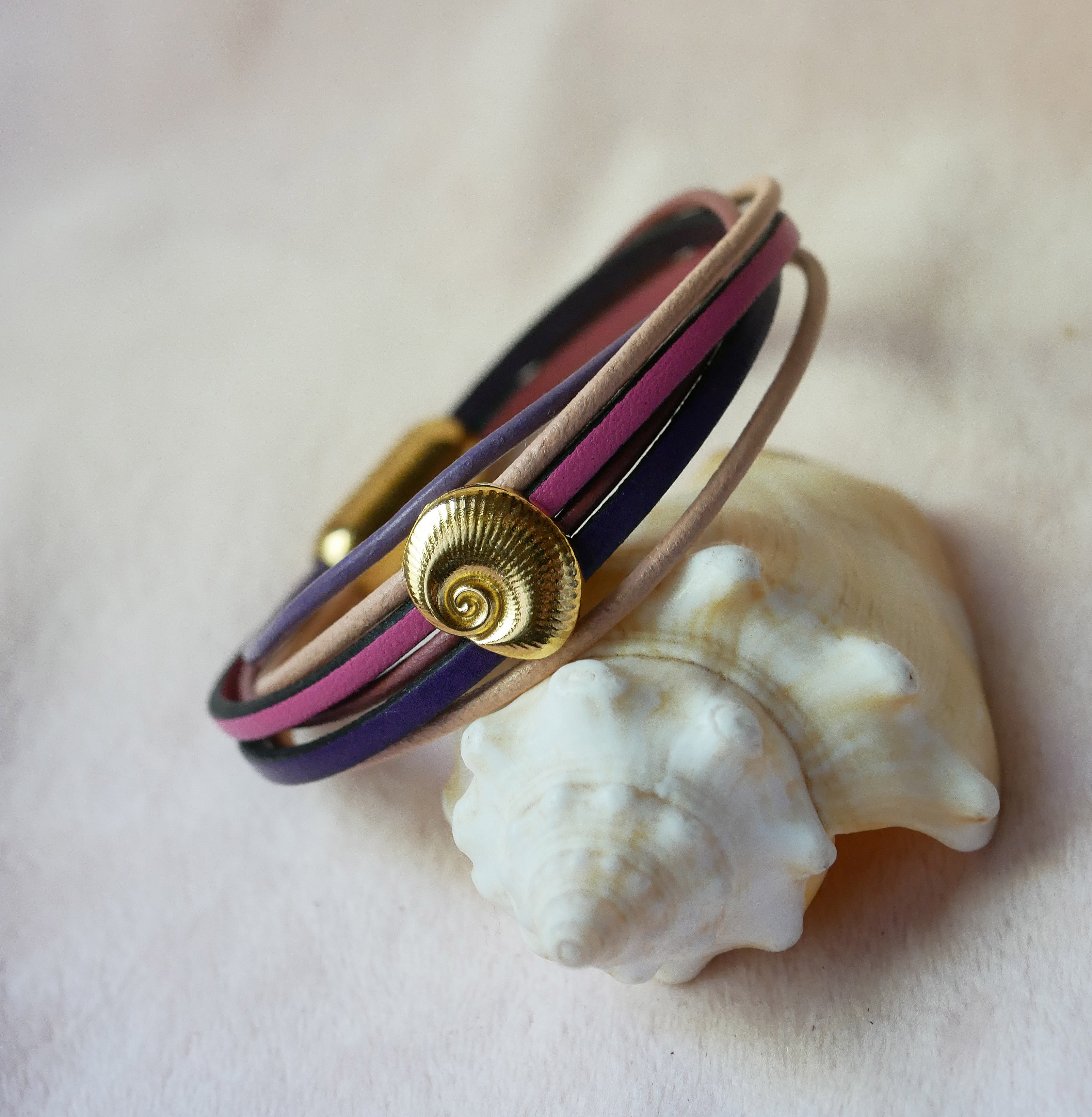 Flerleddsarmb&aring;nd i ferskenfarget og lilla skinn med skjelldekorasjon i gull