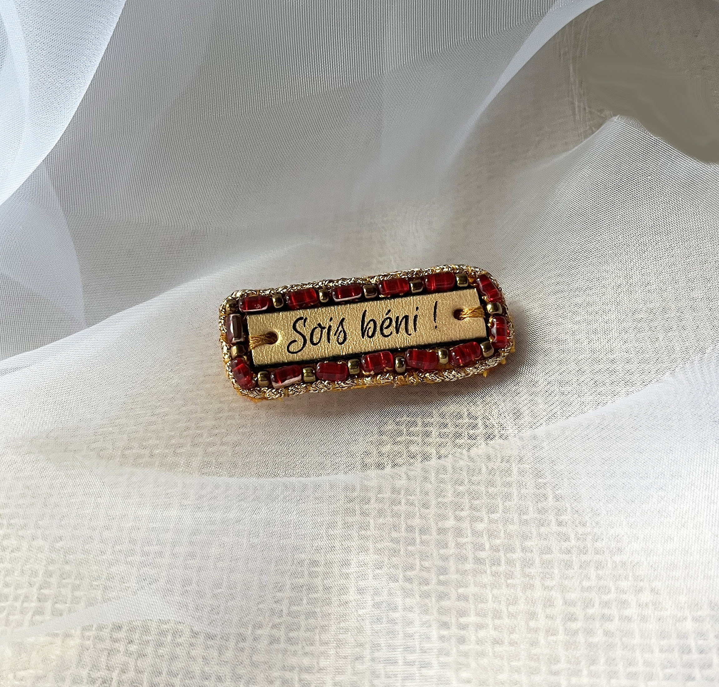Broche &agrave; message en cuir grav&eacute; "sois b&eacute;ni" en perles rouges et dor&eacute;es 