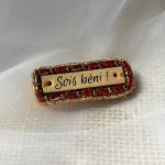 Broche à message en cuir gravé "sois béni" en perles rouges et dorées 